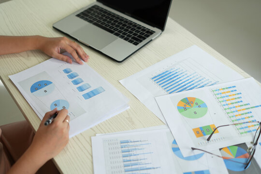 An asian business woman is using laptop at office and checking the financial graph reports showing results about the investment and planning process of her successful real estate business growth on.	
