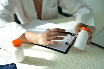 An asian young doctor is holding an medicine bottle to assess the quality of medicine and recommending medication and treatment to patient and explaining the dose and description of the medication.