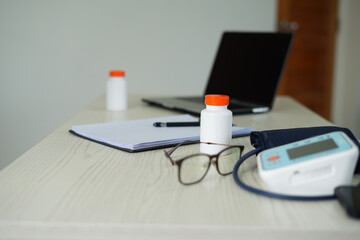 Professional doctor's office table interior with medical equipments, medicine and healthcare concept. Medical examination room with laptop, medication, blood pressure monitor and medical repor