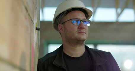 Construction worker in hard hat gazing thoughtfully to the side, standing indoors on construction...