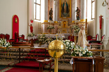 Catholic church interior with golden baptismal font, Virgin Mary statue, and floral decorations