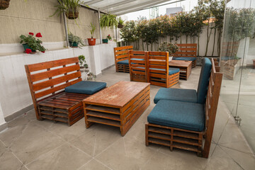 A cozy lounge-style terrace with wooden chairs, cushioned seats, and small round tables under a canopy, creating a relaxed corner for conversations and coffee.

