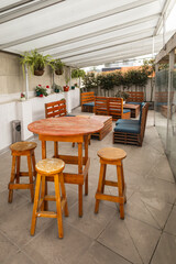 A charming rooftop terrace with rustic wooden dining tables and chairs, surrounded by plants and shaded by a canopy for comfort and style.

