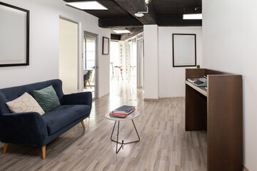 A stylish waiting room featuring a vibrant blue sofa paired with a sleek metal plant stand, creating a modern and aesthetic atmosphere for visitors.

