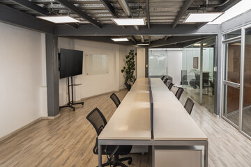 A sleek black office chair sits at a long white conference table in a bright, modern meeting room designed for teamwork and professional discussions.


