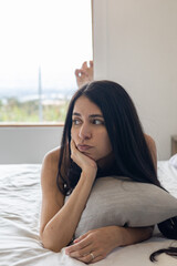 Lying face down with arched back and elbows propped, she hugs a pillow, lost in thoughtful worry and quiet contemplation.

