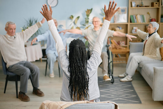 Instructor leading group exercise with senior participants seated in living room setting. Highlighting active engagement, this scene captures enthusiasm and focused commitment