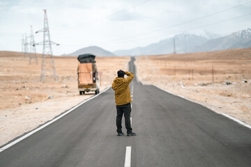 Fototapeta premium Solo traveler standing on an open highway in the high-altitude landscape of Leh Ladakh, surrounded by majestic barren mountains, clear skies, and the serenity of remote Himalayan wilderness