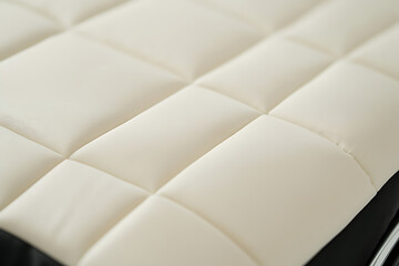 Obraz premium Detailed close-up of a creamy white, quilted surface with diamond-pattern stitching, creating a soft, padded texture. Perfect for backgrounds or textures.