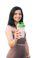 Athletic young woman in sportswear holding shaker with protein cocktail, focus on a shaker in foreground, isolated on a white background