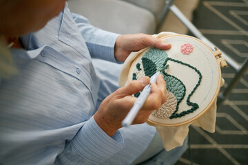 Close-up photo capturing person embroidering intricate design on fabric. Focus is on detailed needlework and careful placement of threads, creating vivid patterns