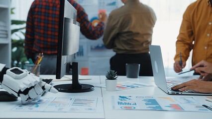 A dynamic office scene showcasing teamwork as diverse professionals engage in brainstorming, analyzing data on charts, and utilizing digital devices for effective collaboration.Noogenesis