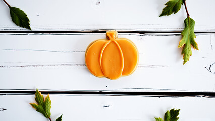 Pumpkin shaped cookies on white wooden surface with green leaves