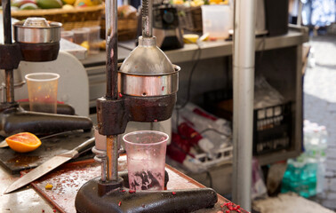 Manual citrus juicer with fresh oranges and spilled juice on a vibrant market stall