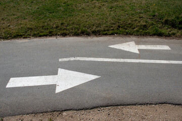 Two white directional arrows painted on asphalt indicate traffic flow in a European road setting,...