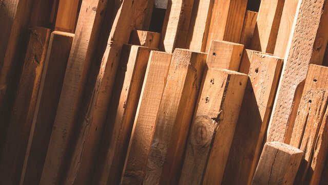 The old wood timbers group leaning against the wall inside of storage house with light and shadow on surface, remaining wooden material used for reuse and recycling concept