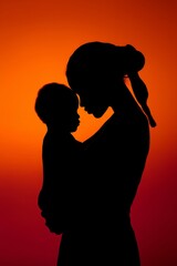 Silhouette of a woman holding a baby against an orange and red gradient sunset backdrop. Portrait of motherhood with strong bond.