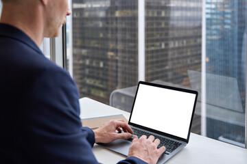Business man using laptop in office sitting at desk. Male hands typing on computer white blank mock up empty screen display for business websites or services ads. Over shoulder view. Close up.