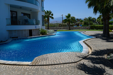 Outdoor swimming pool beside a white house in a sunny residential complex in Cyprus.