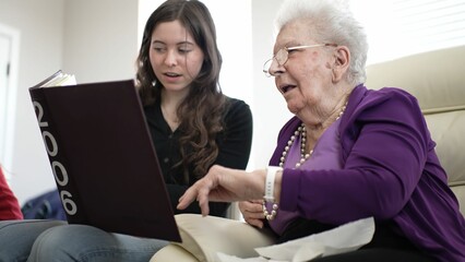 Grandmother and granddaughter enjoy a special moment looking through a family album, reflecting on...