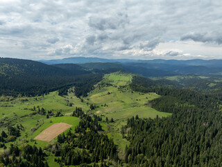 Naklejka premium Aerial view of lush green valleys and forests under a cloudy sky showcasing the natural beauty of the landscape