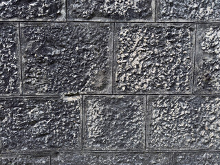Fototapeta premium Close up of a dark textured stone wall featuring square blocks with weathered surfaces and defined joints