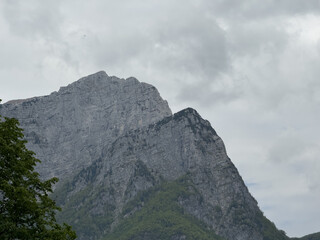Massive gray mountain under a cloudy sky Natural scenery featuring rock face and tree branches in the foreground