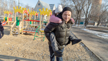 Grandfather playing with her granddaughter on the playground in the park in winter