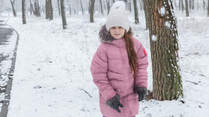 Little girl in colorful clothes play outdoors during a snowfall.