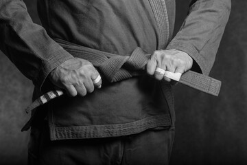 male hands tighten the tied belt on a sports kimono for martial arts jiu jitsu, black and white