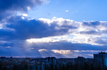 Dramatic dark-blue sky and rays of sun breaking through the clouds against the backdrop of the city. Selective focus.