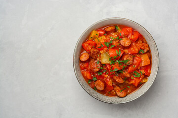 Traditional Hungarian dish Lecho or Lecso or Letscho. Stew with peppers, tomatoes, onions and sausages in bowl on concrete background.