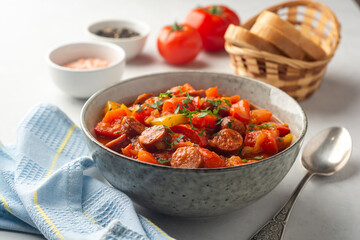 Traditional Hungarian dish Lecho or Lecso or Letscho. Stew with peppers, tomatoes, onions and sausages in bowl on concrete background.