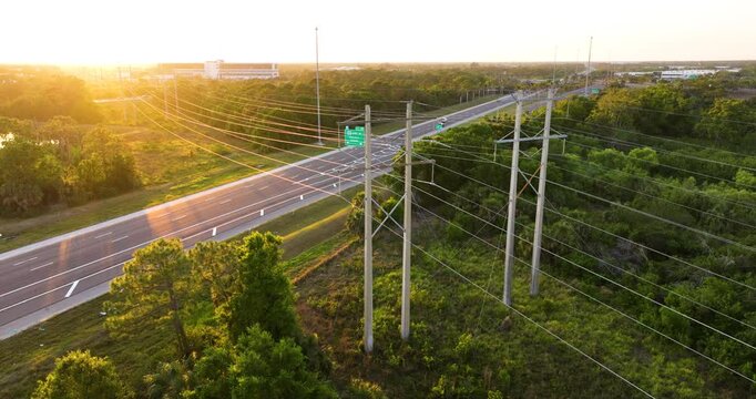 Electric transmission towers with high voltage lines crossing above highway traffic. Infrastructure concept for energy distribution and road network.