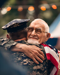 A soldier hugging an elderly man with glasses and an american flag draped over his shoulders outside