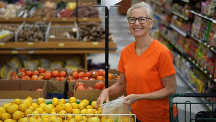 Slow motion portrait of smiling happy pretty mature woman selecting lemons in a grocery store.