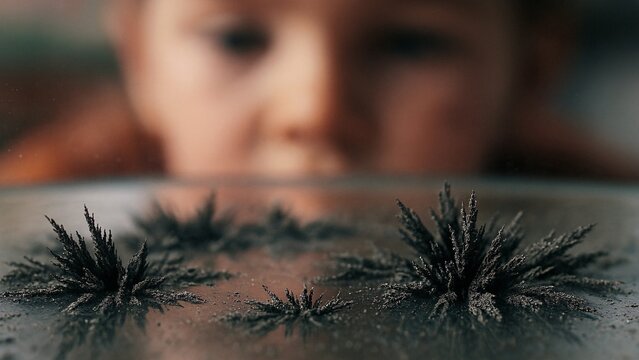 Curious child scientist observing magnetic field lines visualized with iron filings on a glass surface, exploring the wonders of physics and magnetism