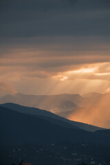 Fototapeta premium Mountain layers under a dramatic sunset sky Beams of light pierce through clouds illuminating the peaks