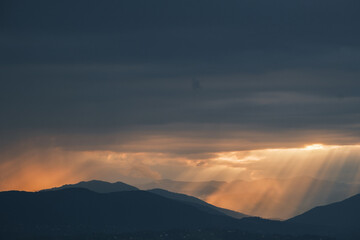 Dramatic mountain range silhouette with sun rays piercing through the heavy clouds creating a serene and powerful landscape