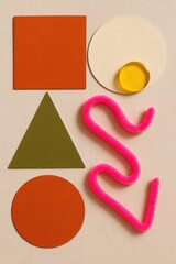 Brightly colored geometric shapes and a pink pipe cleaner create a playful composition, perfect for educational and creative design projects.