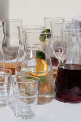 Glass jugs with water, lemon, mint and juice on a white table in sunlight. Refreshing summer drinks served outdoors, perfect for event, party or restaurant design use.