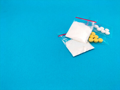 clear plastic bags display various pills and powders drugs on a blue background. 