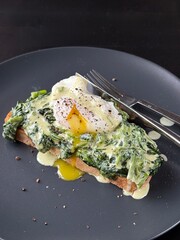 Poached egg on a piece of bread with spinach on the black plate