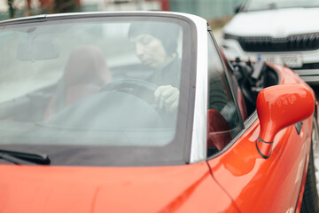 A person is driving a vibrant red convertible through the bustling environment of a modern city,...