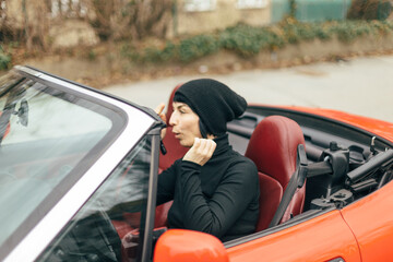 A woman dressed in a stylish black outfit is carefully applying her makeup while seated in a...