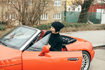 A person is comfortably seated in a vibrant orange convertible, proudly showcasing the essence of...