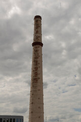 A tall chimney stack rises prominently in a sprawling industrial area, set against a backdrop of an...
