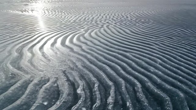 Frozen arctic beach with rippled sand patterns and snow covered mountains under a hazy winter sky landscape in a remote location