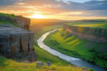 Naklejka premium A winding river flows through a lush green canyon at sunset, casting a golden glow over the landscape and scenic vista.