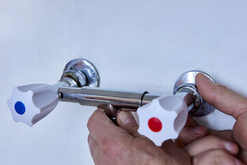 Hands are installing new two handle faucet onto wall outlets, plumber tightens metal fixture with...